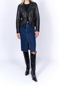 Svart lädermotorcykeljacka över en figursydd svart topp, kombinerad med en knä-lång blå denimkjol och högklackade svarta stövlar.