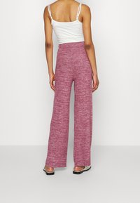 Rosa, stickade vida byxor med ett texturerat mönster, hög midja och lös passform, ihop med en åtsittande vit topp och platta sandaler.