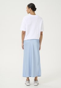 Hvid kortærmet t-shirt parret med en lyseblå maxi-nederdel. Nederdelen har en glat tekstur, er ankel-lang og bæres med hvide sneakers.