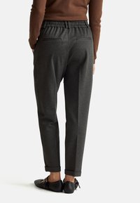 Uhlově šedé kalhoty uvolněného střihu s elastickým pasem, ohrnutými manžetami a zadními kapsami, v kombinaci s černými plochými botami.