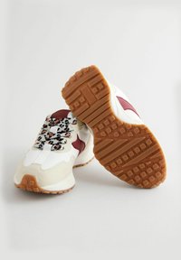 Sneakers z białą i beżową górą, burgundowymi akcentami, sznurówkami w panterkę oraz teksturowaną, brązową gumową podeszwą.