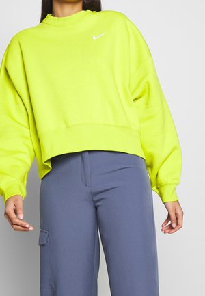 Felpa verde neon con taglio cropped, maniche oversize e logo Nike bianco sul petto. Abbinata a pantaloni cargo grigi.