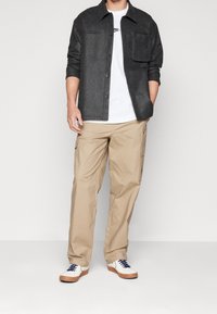 Dark gray button-up shirt with a chest pocket, paired with beige cargo pants and white sneakers with blue accents. Casual fit and texture.