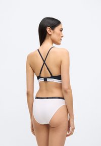 Czarny i szary sportowy biustonosz z krzyżującymi się ramiączkami, z elastyczną opaską z logo marki. Białe figi hipsterskie z pasującym logo na pasku.