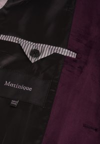 Burgundijos kostiumo švarkas su satino tekstūra, juoda vidinė danga, dryžuotas kišenės dekoras ir etiketė su įrašu "Matinique" viduje.