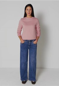 Světle růžová dlouhá košile s kulatým výstřihem, spojená s širšími modrými džíny. Oblečení doplňují tmavě hnědé boty.