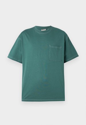 T-shirt teal à manches courtes avec des coutures blanches et une poche sur la poitrine du côté gauche, présenté sur un fond blanc uni.