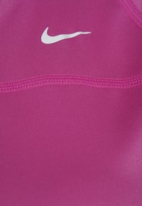 Haut de sport rose en tissu lisse et extensible avec un léger éclat, orné d'un petit logo Nike blanc près de l'encolure.