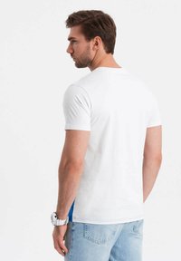 Bílý bavlněný tričko s krátkým rukávem, s modrým bočním panelem. Vybavené světle modrými džíny. Jednoduchý design s kulatým výstřihem.