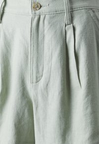 Světle zelené lněné šortky s knoflíkovým zapínáním, sklady a bočními kapsami. Tkanina má měkký, strukturovaný vzhled.