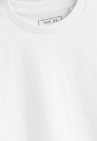 T-shirt blanc à col rond avec col côtelé affichant une étiquette imprimée à l’intérieur du col mentionnant "next.82".