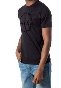 Camiseta de algodón negra con cuello redondo, mangas cortas y un diseño de logo en la parte delantera en un formato circular. Combinada con jeans de mezclilla azules.