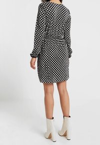 Schwarzes Kleid mit wei�ßen Punkten, langen Ärmeln, geraffter Taille und einem strukturierten Stoff. Kombiniert mit weißen Ankle-Boots.