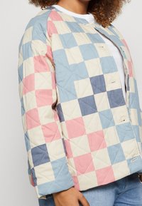 Pikowana kurtka w pastelowych kolorach, z wzorem patchworkowym w różowym, niebieskim i kremowym. Okrągły kołnierz z widocznymi zatrzaskami.