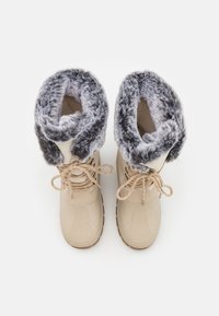 Bottes d'hiver beiges avec des cols en fausse fourrure épais gris et blanc et des lacets beiges, montrées de dessus sur un fond blanc.