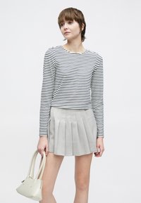 Czarna i biała, pasiasta bluzka z długim rękawem, zestawiona z jasnoszarą plisowaną spódnicą. Nosi małą kremową torebkę z dwoma uchwytami.