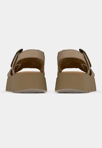 Brown platform sandals featuring a wide strap with a gold-tone buckle, soft suede texture, and a durable rubber sole with ridged edges.