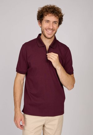 Polo bordeaux à manches courtes, col zippé, texture lisse et accents côtelés. Assorti avec un pantalon khaki clair.