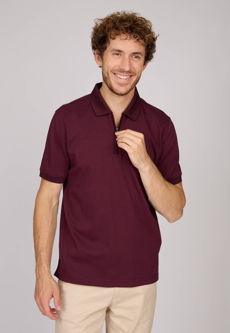 Polo bordeaux à manches courtes, col zippé, texture lisse et accents côtelés. Assorti avec un pantalon khaki clair.