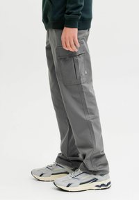 Sive hlače od krpa s dva bočna džepa, opušten fit i glatka tekstura, uparene sa sivim i tamnoplavim tenisicama.