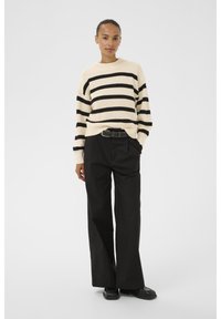 Cream sweater with black horizontal stripes, ribbed texture, and a round neckline. Paired with loose black trousers and black shoes.