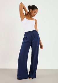 Μπλέ παντελόνι σε ίσια γραμμή με ελαστική μέση, φτιαγμένο από μαλακό ύφασμα. Συνδυασμένο με λευκή εφαρμοστή μπλούζα χωρίς μανίκια.