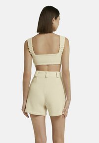 Crème-kleurige twee-delige set met een textuur, geweven bralette met ruches op de schouderbanden en hoge shorts met accentstiksels en riemlussen.