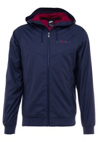 Marine windbreaker met een rode voering in de capuchon, ritssluiting, elastische manchetten en een logo met "BARÇA" in levendige kleuren op de borst.