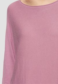 Maglietta a maniche lunghe rosa chiaro con scollatura ampia, caratterizzata da una morbida texture a coste e una vestibilità rilassata. Nessun motivo o hardware visibile.