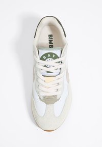 Sneaker bianco e beige con punta in suede texturizzato, pannelli in rete e un adesivo verde sul linguetta. Presenta lacci chiari e suola in gomma.