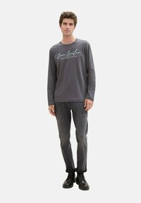 Long-sleeve gray shirt with white text, paired with dark gray jeans and black lace-up boots. Smooth texture, casual fit, and minimalist design.