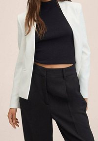 White blazer with notched lapels over a fitted black ribbed crop top, paired with high-waisted black trousers. Smooth texture throughout.