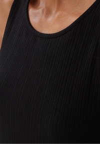 Närbild av en person som bär en ärmlös, rippad svart topp med rund halsringning.