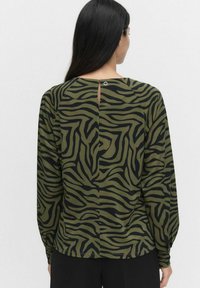 Långärmad topp i olivgrön tyg med svarta zebra-randningar, med en nyckelhålsdetalj i ryggen och avslappnad passform.