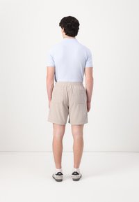 Pantalones cortos de rayas beige con cintura elástica, dos bolsillos traseros y un corte holgado, combinados con una camiseta polo de color azul claro.