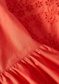 Tessuto rosso con un motivo ricamato che presenta fiori e spirali. Include un orlo arricciato per aggiungere texture. Finitura liscia e intrecciata.