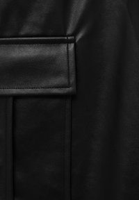 Tissu en cuir noir à texture lisse, présentant une poche à rabat proéminente et des coutures détaillées le long des bords.