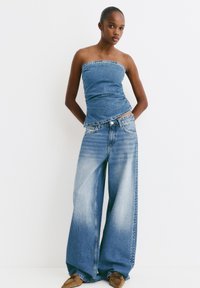 Denim top bez ramienok skombinovaný s širokými denimovými nohavicami. Svetlomodrá farba, zvýraznená kontrastným šitím a bočnými ozdobami.