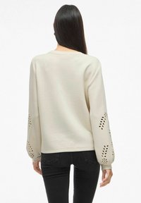 Felpa color crema con maniche lunghe a palloncino e motivi a foglia intagliati. Tessuto morbido e vestibilità rilassata. Design classico con collo a girocollo.