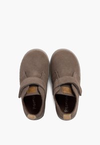 Brązowe zamszowe buty z okrągłym noskiem, regulowanym rzepem i kontrastującymi akcentami w kolorze tan. Płaska gumowa podeszwa, minimalistyczny design.