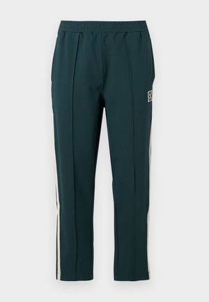 Pantalon de sport vert foncé avec taille élastique, bandes verticales beiges sur les côtés, et petit logo blanc sur la cuisse droite.