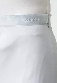 Světle šedá sukně s skrytým postranním zipem a prošitou pasovkou s embosovaným logem Calvin Klein.