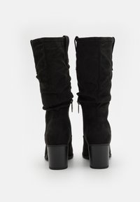 Bottes montantes en daim noir avec un design flou, dotées de deux zips à l'arrière et d'un talon épais noir. Texture lisse et ajustement flexible.