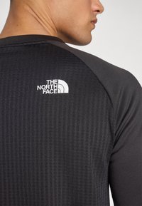 Zwart sportshirt met ribbeltextuur, met een wit logo op de bovenrug. De mouwen zijn raglanstijl en slim fit.