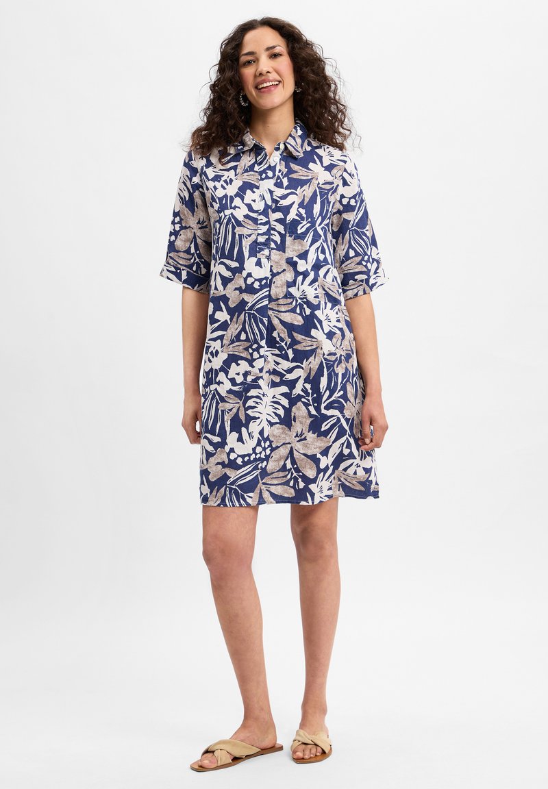 Blaues Knopfhemdkleid mit floralen Mustern in Weiß und Beige, kurze Ärmel, entworfen für eine lockere Passform, bis über das Knie reichend. Weicher Stoff.