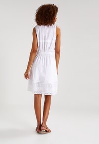 Vestido blanco sin mangas con encaje en el dobladillo, cintura con fruncido y tejido suave. Combinado con sandalias sencillas.