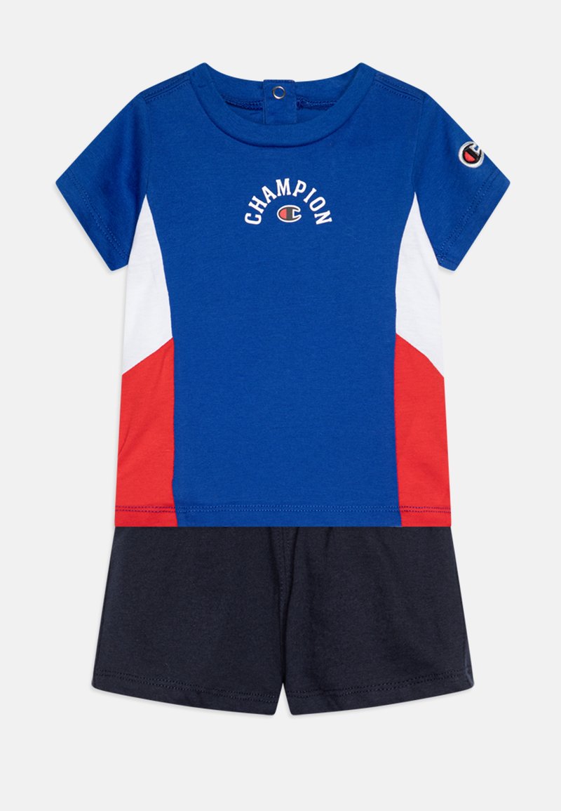 Chemise bleue à manches courtes avec des accents blancs et rouges, arborant le logo "CHAMPION". Associée à un short bleu marine, en coton, coupe décontractée.