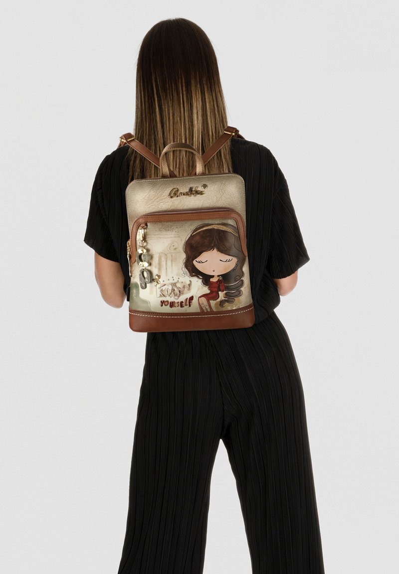 Rucksack mit gold texturierter Außenseite, braunem Boden und verspieltem Charakterdesign mit dem Spruch "Sei du selbst." Enthält dekorative Anhänger.