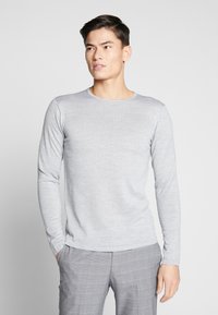 Langermet grå t-skjorte i et glat, mykt stoff, med rund hals og tettsittende silhuett, kombinert med lysegrå rutete bukser.