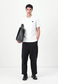 Čierna kožená taška, biele polo tričko s modrým logom, čierne voľné nohavice a čierne topánky. Jednoduchý dizajn a minimalistická farebná paleta.